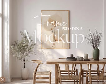 May include: A framed art print with a floral design hangs above a wooden dining table. The room is decorated with a vase of dried branches, a potted plant, and wooden chairs. The text "Frame Mockup PSD DIN A" is visible.