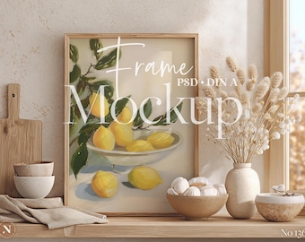 May include: A framed art print featuring a still life of lemons in a white bowl, with green leaves. The frame is light brown. The image is part of a mockup with the word "Frame Mockup" in white script. Other decor includes bowls and a vase.