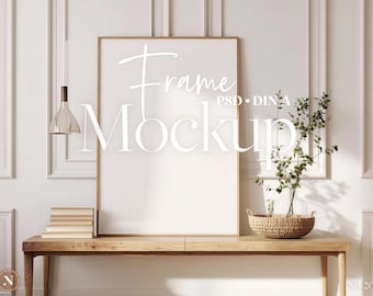 Puede incluir: Una maqueta de marco vertical con el texto "Frame Mockup" en blanco. El marco está sobre una mesa de madera con una pila de libros y una cesta tejida con vegetación. Una lámpara colgante cuelga sobre la mesa.