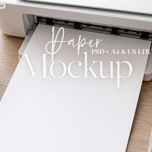 May include: A white printer with a blank sheet of paper extending from the tray. The text Paper Mockup PSD A4 & US LTR is overlaid on the paper. The printer is positioned on a wooden surface with a small bowl of white flowers and a notebook nearby.