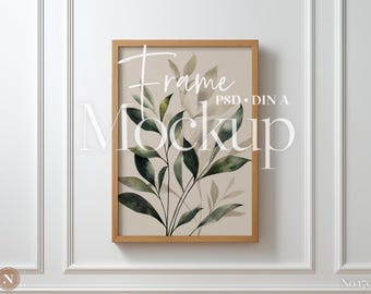 May include: A rectangular framed art print featuring a botanical illustration of green and beige leaves on a light tan background. The frame is made of light brown wood. The words "Frame Mockup" are written on the print.