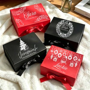 Könnte beinhalten: Vier rechteckige Geschenkboxen mit Deckel und Schleifenverschluss. Zwei sind rot mit weißen Weihnachtsmotiven und den Namen Sara und Lackie. Zwei sind schwarz mit weißen Motiven und den Namen Irish und Jeremiah. Jede Box trägt die Aufschrift Christmas Eve Box.