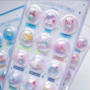 May include: A sheet of stickers featuring miniature desserts inside clear capsules. The stickers include ice cream, jelly, and candy, with labels like "ice cream," "jelly," and "ice candy." The sheet is decorated with stars and the text "COLLECT CAPSULE STICKERS."