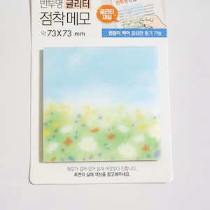 May include: A square translucent sticky note pad featuring a printed landscape of a blue sky above a green meadow filled with small white, yellow, and orange flowers. The packaging includes the text 73X73 mm and Korean characters.
