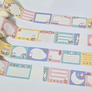 Könnte beinhalten: Dekoratives Washi-Tape mit einem sich wiederholenden Muster aus farbenfrohen rechteckigen Etiketten mit Hasenillustrationen. Die Etiketten haben verschiedene Designs, darunter leere Bereiche, Linien und Rastermuster, in Pastellfarben.