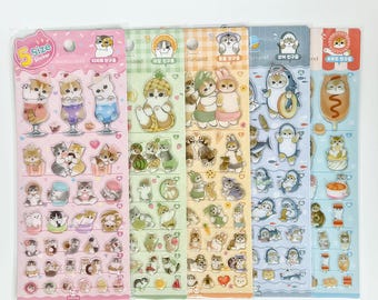 May include: A collection of five sticker sheets featuring adorable cartoon animals. Each sheet has a different color scheme, including pink, green, yellow, blue, and red. The stickers depict cats, bunnies, penguins, and other cute characters in various poses.