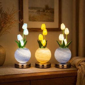 Op de afbeelding: Drie decoratieve tulpenlampen met gloeiende lampen. Elke lamp heeft een ronde, gemarmerde glazen vaas in blauw, geel en blauw, met een metalen voet. De lampen zijn geplaatst op een houten oppervlak, wat een warme, uitnodigende sfeer creëert.