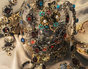 Peut inclure: Une collection de bijoux vintage, comprenant des colliers, des bagues et des bracelets, dans un bocal en verre transparent. Les bijoux présentent des motifs ornés avec des accents rouges, bleus et dorés. Certaines pièces sont exposées à l'extérieur du bocal.