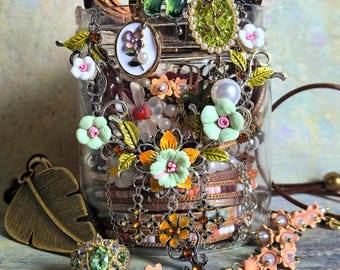 May include: A clear glass jar overflowing with various jewelry pieces. The jewelry includes bracelets, necklaces, rings, and earrings, featuring floral and butterfly designs. The color palette includes gold, green, pink, and white accents.