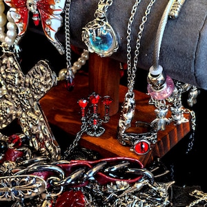 May include: An assortment of gothic-style jewelry, including necklaces, rings, and bracelets. The jewelry features silver-toned metal with red and clear accents. A cross pendant, a butterfly pendant, and a ring with a red eye are visible.