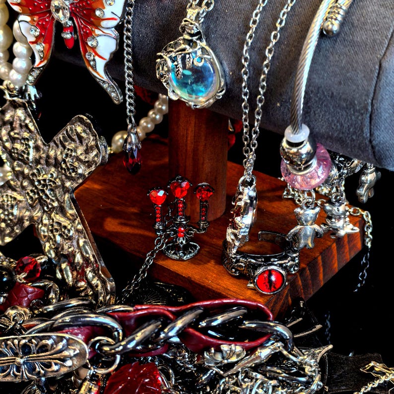 May include: An assortment of gothic-style jewelry, including necklaces, rings, and bracelets. The jewelry features silver-toned metal with red and clear accents. A cross pendant, a butterfly pendant, and a ring with a red eye are visible.