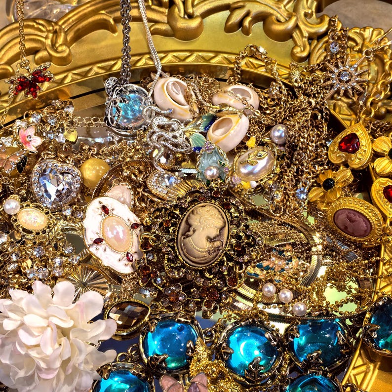 Op de afbeelding: Een verzameling vintage sieraden, waaronder kettingen, hangers en broches, in goudtinten. Het assortiment bevat verschillende edelstenen, parels en camee-ontwerpen. De sieraden zijn gerangschikt op een decoratief gouden dienblad.