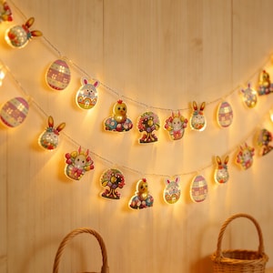 Peut inclure: Guirlande lumineuse sur le thème de Pâques avec des ornements en forme de lapin, de poussin et d'œuf. Les lumières sont suspendues à un fil fin et émettent une lueur chaleureuse. Idéal pour les décorations de Pâques.