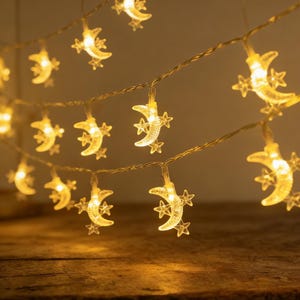 Op de afbeelding: Slingerlichtjes met verlichte halve manen en sterren. De warme, zachte gloed van de lampjes creëert een gezellige sfeer. De lampjes zijn geregen op een dunne, transparante draad, perfect voor het decoreren van een kamer.