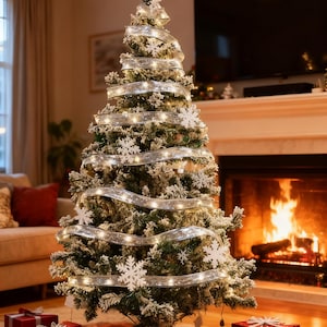 Puede incluir: Un árbol de Navidad decorado con adornos de copos de nieve blancos, una cinta plateada y luces de cadena. Los regalos envueltos en rojo, plateado y blanco están en la base del árbol. Una chimenea con fuego ardiendo está al fondo.