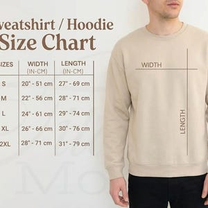 May include: A beige sweatshirt with a size chart. The chart shows measurements for width and length in inches and centimeters for sizes S to 2XL. The sweatshirt is shown on a person, with lines indicating width and length.