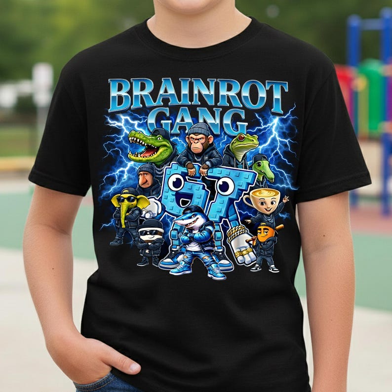 以下が含まれることがあります： 黒いTシャツ。青色の「BRAINROT GANG」の文字と稲妻のグラフィック。ワニ、猿、カエル、サメなどの漫画のキャラクターが描かれています。柔らかい素材で作られたTシャツです。
