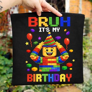 Könnte beinhalten: Schwarze Tragetasche mit einer farbenfrohen Grafik, die eine Lego-Figur mit Partyhut zeigt. Der Text "BRUH IT'S MY BIRTHDAY" wird in leuchtenden Blockbuchstaben zusammen mit Luftballons und Sternen angezeigt.