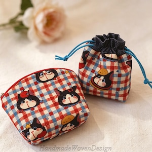 May include: Two fabric pouches with a red, white, and blue plaid pattern and cat illustrations. One is a zippered cosmetic bag, and the other is a drawstring bag. The drawstring bag has a dark blue denim top and light blue drawstrings. The cosmetic bag has a red zipper.