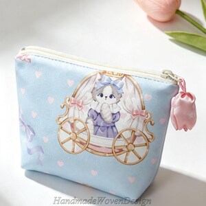 May include: A light blue zippered pouch featuring a printed illustration of a cat wearing a blue bow inside a gold carriage. The fabric is decorated with small pink hearts and light purple ribbons. A pink tulip-shaped charm hangs from the zipper.