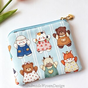 May include: A light blue zippered pouch featuring a repeating pattern of cartoon animals including a sheep in blue overalls, a calico cat in a floral dress, a brown bear in tan overalls, a bear in a polka dot dress, a cow, and a fox.