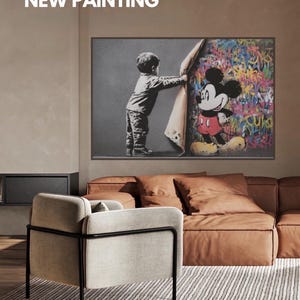 Może przedstawiać: Oprawione dzieło sztuki przedstawiające dziecko odsuwające ścianę, aby odsłonić kolorowego Myszka Miki. Grafika jest wyświetlana nad brązową skórzaną sofą. Tekst "NEW PAINTING" znajduje się u góry obrazu.