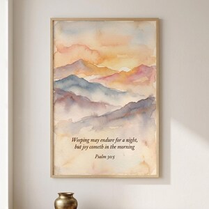 May include: A framed watercolor print featuring a mountain landscape at sunrise with soft hues of orange, pink, and blue. The text reads: Weeping may endure for a night, but joy cometh in the morning. Psalm 30:5. The artwork is displayed in a light wood frame.