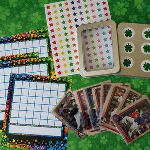 May include: An assortment of craft supplies including baseball cards, star stickers, bingo cards, and a metal tin. The bingo cards have a colorful border and a blue grid. The tin has a clear window and a lid with shamrock stickers.