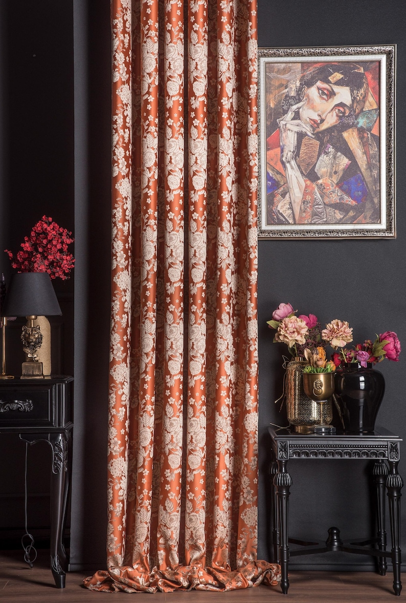 Pu&ograve; includere: Tenda con motivo floreale color ruggine. La tenda presenta un motivo ripetuto di fiori bianchi. Un ritratto incorniciato &egrave; appeso alla parete scura. &Egrave; visibile anche un tavolino nero con una lampada e un vaso di fiori.