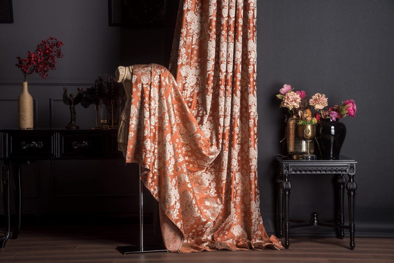 Pu&ograve; includere: Tenda con motivo floreale color ruggine e tessuto drappeggiato abbinato. La tenda &egrave; accanto a un tavolo nero con un vaso di fiori. La stanza ha pareti scure e pavimento in legno. Elementi decorativi: vasi e un tavolino.