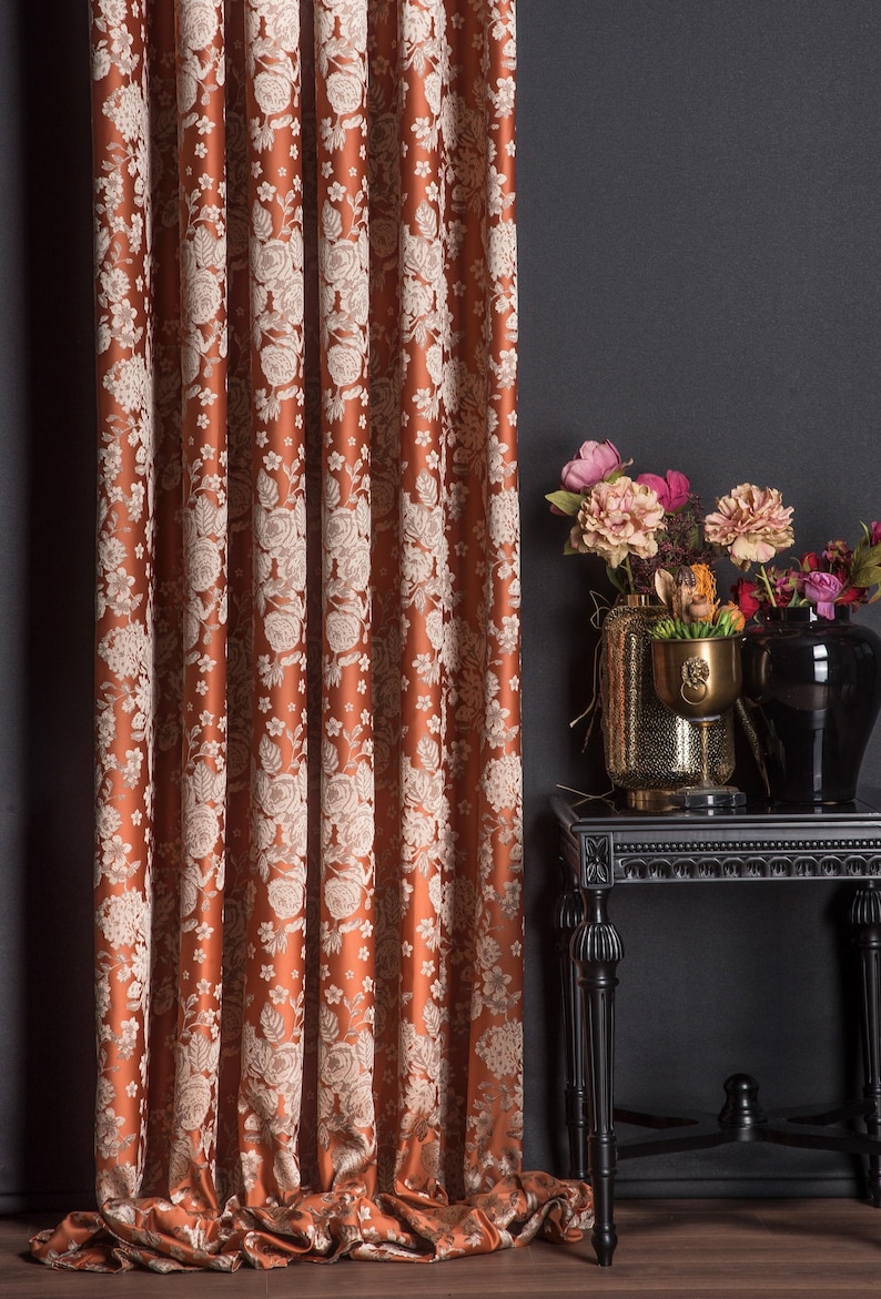 Pu&ograve; includere: Tenda color ruggine con motivo floreale color crema. Il tessuto &egrave; drappeggiato in pieghe verticali, creando un aspetto strutturato. Un tavolino nero con vasi di fiori &egrave; accanto.