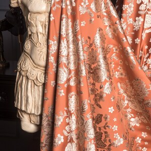 Pu&ograve; includere: Un tessuto drappeggiato color ruggine con un motivo floreale nei toni del bianco e dell'argento. Il tessuto &egrave; drappeggiato su un busto classico. Il design floreale comprende rose e altri fiori, creando un tessuto lussuoso.