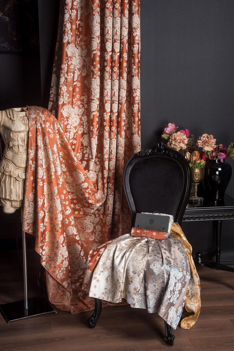 Pu&ograve; includere: Tessuto per tende con motivo floreale color ruggine drappeggiato su una sedia nera. Il tessuto &egrave; drappeggiato anche su una statua e un rotolo di tessuto &egrave; sulla sedia. Un tavolo nero con fiori &egrave; sullo sfondo.