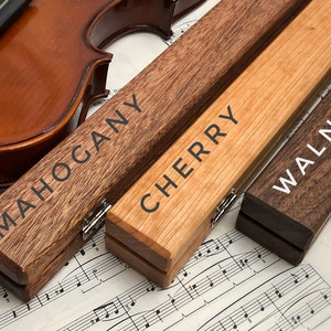 May include: Three wooden violin cases in mahogany, cherry, and walnut wood. The cases are closed and have hinges. The cases are on a sheet of music.