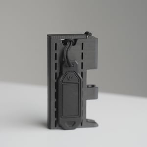 May include: A black, rectangular device with a textured surface and a lanyard. The device has a series of vertical slots and a smaller, attached component. A black cord is looped through the top. The device has a small emblem on the front.