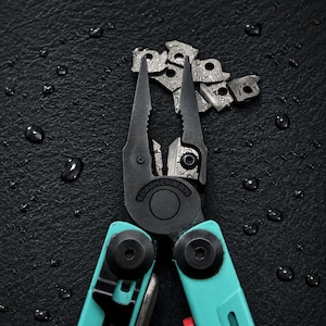 Peut inclure: Un outil multifonction Leatherman doté de pinces noires avec un motif en acier Damas sur les composants de coupe internes. L'outil possède des poignées bleu sarcelle vif fixées par des vis noires. La marque Leatherman est gravée au centre.