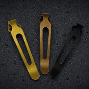 May include: Three elongated metal pocket clips arranged vertically. The left clip is bright gold, the centre clip is a muted bronze, and the right clip is matte black. Each clip features a rounded top with two circular holes and a long central cutout.