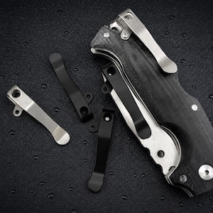Peut inclure: Un couteau de poche pliant avec un manche noir texturé et un clip de poche en métal argenté, accompagné de trois clips de poche de rechange séparés en finitions noire et argentée, chacun doté de trous de montage et d'un design incurvé.