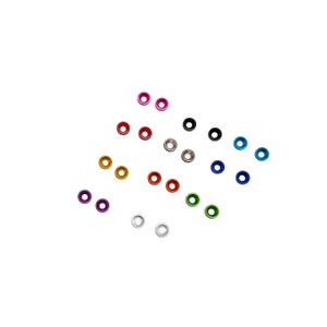 May include: A selection of small, brightly coloured metal eyelets in shades such as pink, red, black, blue, green, gold, and silver. These eyelets are circular with a central hole, and are scattered on a white backdrop.