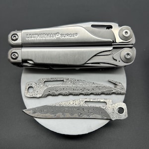 May include: A multi-tool with the text "LEATHERMAN SURGE" is shown closed, with two additional blades. The blades have a unique patterned design. The tools are silver in color.