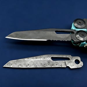Könnte beinhalten: Ein Multitool mit einer teilweise gezahnten Klinge und einer separaten gemusterten Klinge, beide in dunkler Ausführung. Das Multitool hat einen türkisfarbenen Griff. Die Klingen werden vor einem dunkelblauen Hintergrund gezeigt.