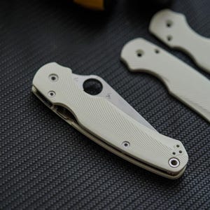以下が含まれることがあります： 斜めのテクスチャパターンが施されたオフホワイトのハンドルを持つ折りたたみ式ポケットナイフ。ブレードには円形のサムホールがあり、さらにネジ穴があらかじめ開けられた2枚のオフホワイトのハンドルスケールが付属しています。