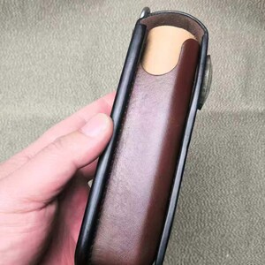 Puede incluir: Un estuche de cuero marr&oacute;n con ribete negro y cierre met&aacute;lico. El estuche rectangular est&aacute; dise&ntilde;ado para guardar un objeto peque&ntilde;o. El interior es de color beige claro.