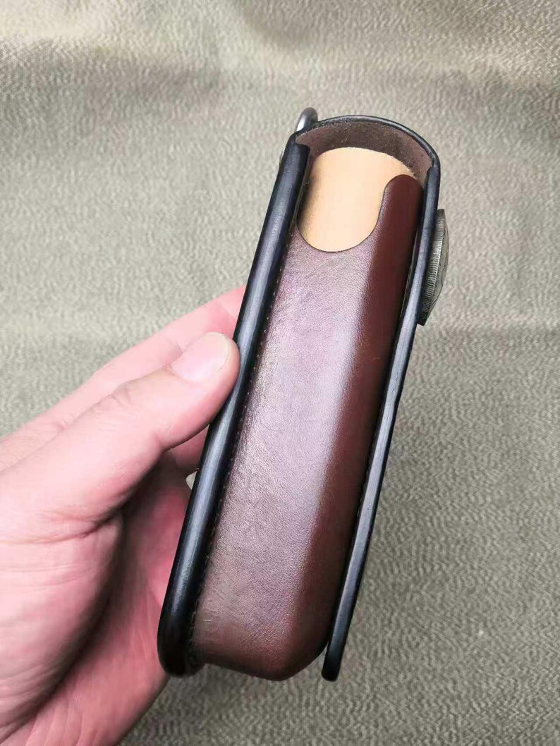 Puede incluir: Un estuche de cuero marr&oacute;n con ribete negro y cierre met&aacute;lico. El estuche rectangular est&aacute; dise&ntilde;ado para guardar un objeto peque&ntilde;o. El interior es de color beige claro.