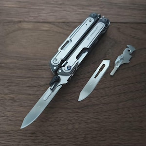 May include: A multi-tool with a silver finish, featuring a knife blade, a saw blade, and other tools. The multi-tool is partially open, displaying the knife blade. The image also shows a separate blade and a small tool. The text "LEATHERMAN ARC" is visible.
