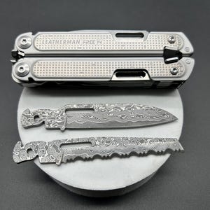 Könnte beinhalten: Ein silbernes Multitool mit der Aufschrift "LEATHERMAN FREE P4" und zwei zusätzlichen Klingen. Das Multitool hat eine strukturierte Oberfläche. Die Klingen haben ein einzigartiges Muster. Die Artikel werden auf einer grauen Oberfläche präsentiert.