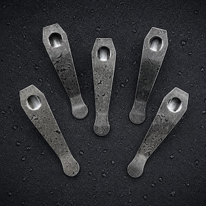 May include: Five metal pocket clips with a dark, mottled, and textured finish. Each clip features a tapered shape, a rounded end, and a circular hole at the wider top section. The surface displays a complex, swirling pattern in shades of gray.