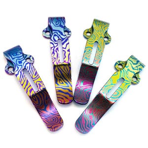 Puede incluir: Cuatro clips de bolsillo coloridos con patrones arremolinados únicos. Cada clip presenta un esquema de color diferente, incluyendo azul, amarillo, morado y rojo, con un diseño texturizado en forma de onda. Los clips tienen forma rectangular con una parte superior curvada y un recorte central.