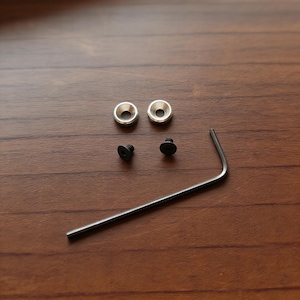 May include: A collection of small hardware components, including two silver washers, two black screws, and a silver Allen wrench. The items are arranged on a wooden surface, providing a neutral backdrop for the tools.