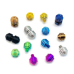 May include: A collection of colorful, metallic beads in various shapes and sizes. The beads are in shades of gold, silver, blue, green, purple, and black. The designs include spiral and ribbed patterns, with some having screw-like features.